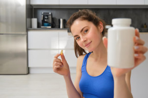 close-up-portrait-young-woman-fitness-instructor-showing-bottle-vitamins-taking-buds_1258-218249