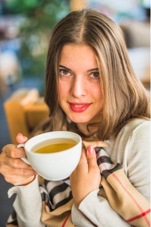smiling-young-woman-showing-herbal-tea-white-cup_23-2147975425
